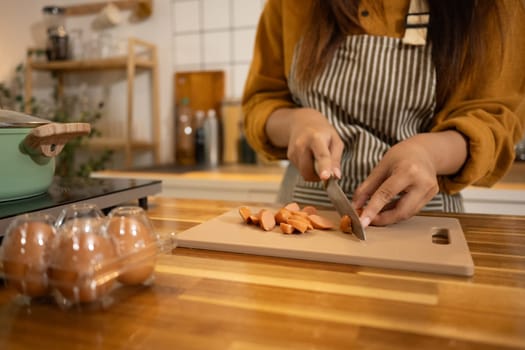 Close up of woman chopping sausages for a quick meal at wooden kitchen counter.