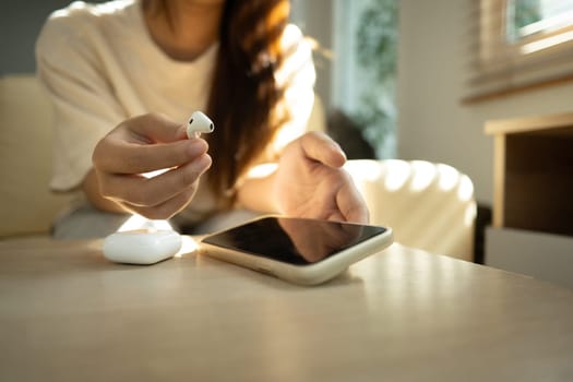 Close up shot of smiling woman connecting wireless earbuds to smartphone.