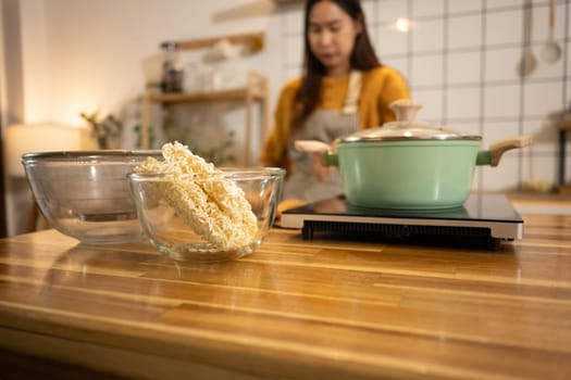 Glass bowl filled with dry instant noodles on a wooden countertop, ready to be cooked.