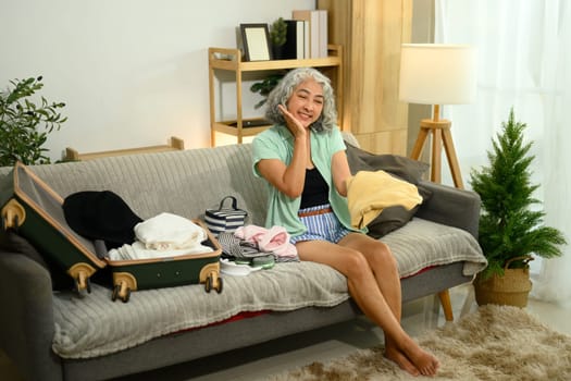 Happy senior woman packing clothes for a summer vacation.