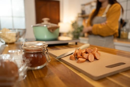 Close up of sliced sausages, sauce, and other ingredients on a wooden kitchen counter.