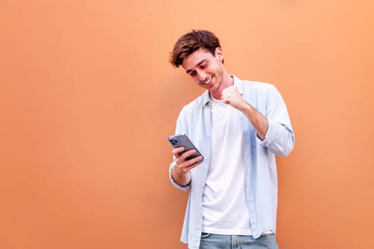 young man holding cell phone and smiling happy while celebrating , concept of positivity and enjoyment of technology, copyspace for text