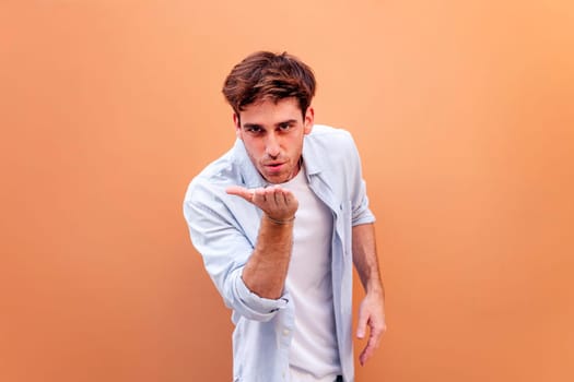 young man giving a kiss with hand while smiling looking at camera in a positive and friendly mood, concept of love, copyspace for text