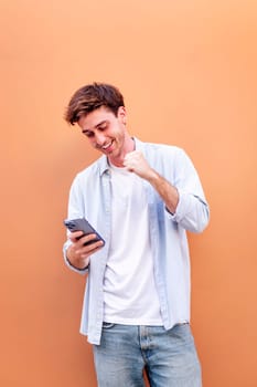 young man holding cell phone and smiling happy while celebrating, concept of positivity and enjoyment of technology, copyspace for text