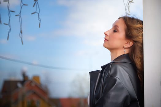 A woman leans against a pillar, closing her eyes peacefully as she savors the warm sunlight and fresh air.
