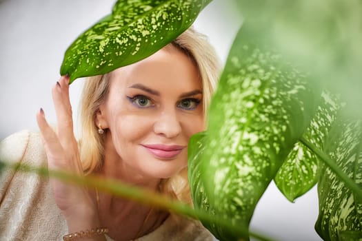 A middle-aged woman engages with a lively indoor plant while enjoying a creative moment during a blogging session.