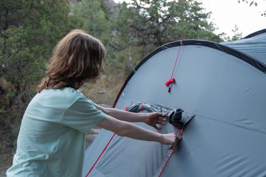 Young caucasian boy pitching grey tent on camping trip with camping equipment