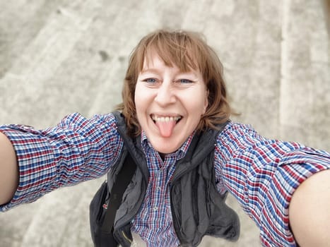 A middle-aged woman with blonde hair happily takes a selfie, capturing her joyful spirit during her travels.