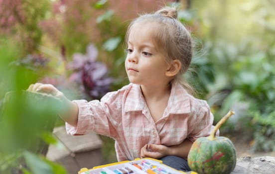 A young child paints a small pumpkin outside, surrounded by nature. This image captures the simplicity and joy of seasonal creativity.