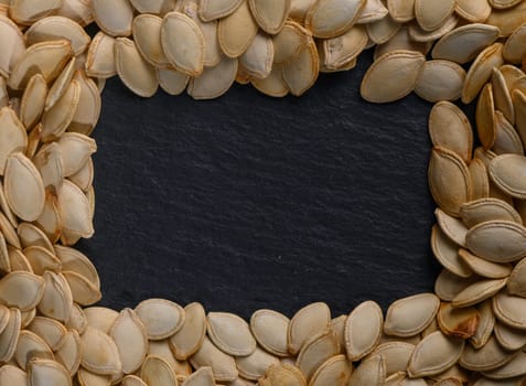 Artful arrangement of dried pumpkin seeds forming a unique border on a dark slate surface, perfect for seasonal decor.