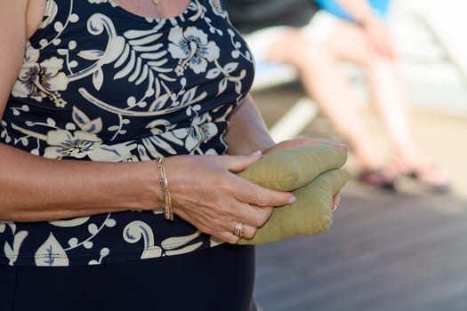 Energetic composition of hands clutching bean bags during a cornhole match, showing details like jewelry, floral design, and summer warmth.