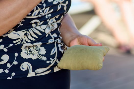 Close-up image of a woman hands holding bean bags for cornhole, with a patterned shirt and bracelet adding unique character to the moment.