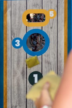 A woman with braided hair intensely prepares to throw the bean bag during a lively cornhole match, showcasing athleticism and focus.