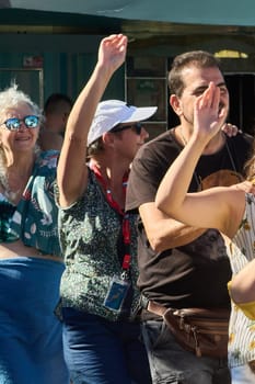 Catania. Italy - March 11, 2025: Cheerful individuals gathered outdoors, raising hands energetically while enjoying collective recreation under a bright sunny day.