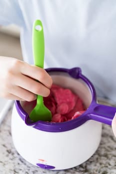 Eager eyes focus on the pot of vibrant, melting candy as a young cook gently swirls the mixture, poised to transform plain snacks into delectable treats.