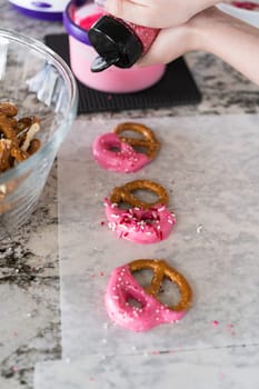 Freshly dipped and still glistening, these crunchy pretzels are lovingly adorned with pink chocolate and a scattering of colorful sprinkles, promising a feast for the senses.