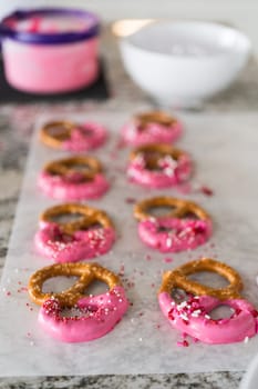 Freshly dipped and still glistening, these crunchy pretzels are lovingly adorned with pink chocolate and a scattering of colorful sprinkles, promising a feast for the senses.