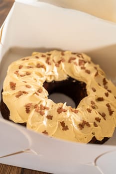 Carefully placing the gingerbread bundt cake, adorned with salted caramel frosting and gingerbread sprinkles, into a white paper bundt cake box with a clear window for gifting.
