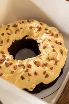 Carefully placing the gingerbread bundt cake, adorned with salted caramel frosting and gingerbread sprinkles, into a white paper bundt cake box with a clear window for gifting.