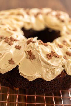 A gingerbread bundt cake being generously frosted with salted caramel frosting and topped with delightful gingerbread sprinkles.