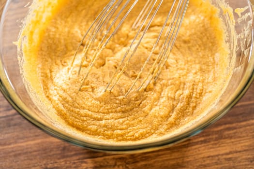 In a glass mixing bowl, a large hand whisk expertly blends the ingredients for a delectable gingerbread bundt cake with caramel frosting.