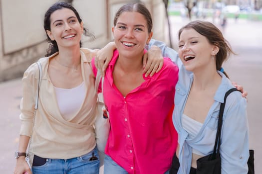 three happy gossipy teenagers chatting outdoors. A group of Caucasian friends chatting and communicating. Young adult students smiling and walking together at a social gathering.