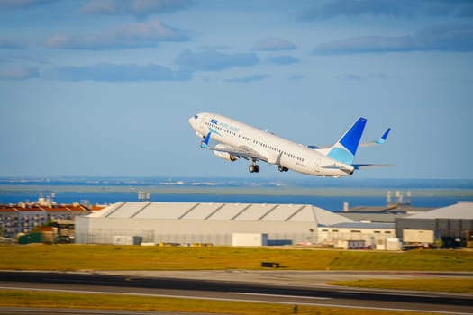 Lisbon, Portugal - Apr 29, 2024: Panning shot of ASL Airlines Boeing 737 aircraft during takeoff from Lisbon airport runway. Cityscape, river view in background, airport warehouse facility, clear blue skies on sunny day. Blurred background.