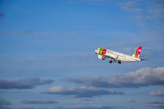 Lisbon, Portugal - Apr 29, 2024: TAP Air Portugal Airbus 320 shot mid-flight, ascending into clear blue sky with some clouds after takeoff on sunny day. Air traffic, vacations, travel, destinations, aircraft, international aviation, commercial airlines