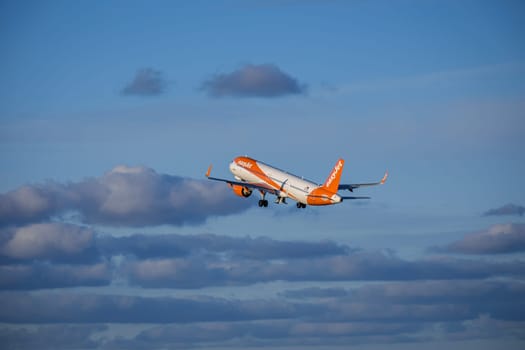 Lisbon, Portugal - Apr 29, 2024: EasyJet Airbus 321 neo aircraft shot mid-flight, ascending into clear blue sky with some clouds after takeoff on sunny day. Air traffic, vacations, travel, destinations, aircraft, low-cost airline, commercial flight
