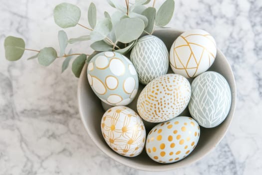 A stylish minimalist Easter centerpiece showcases beautifully decorated golden patterned Easter eggs arranged in a bowl. Eucalyptus leaves accent the display, set against a chic marble countertop.