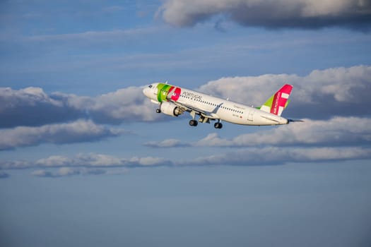 Lisbon, Portugal - Apr 29, 2024: TAP Air Portugal Airbus 320 shot mid-flight, ascending into clear blue sky with some clouds after takeoff on sunny day. Air traffic, vacations, travel, destinations, aircraft, international aviation, commercial airlines