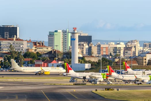 Lisbon, Portugal - Apr 24, 2024: TAP and Vueling airplanes parked at Lisbon airport on sunny day, clear skies and city view in background. Planes being serviced and prepared for flights, air traffic control tower and runway, travel destination