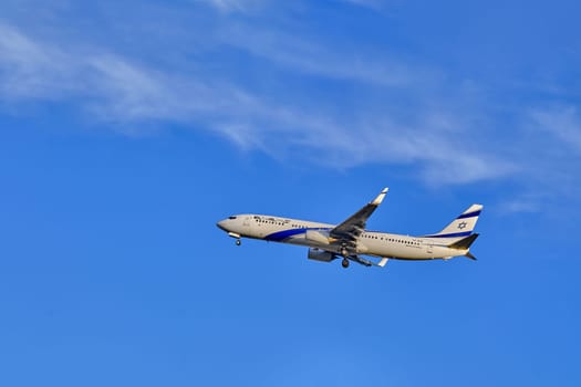 Lisbon, Portugal - Jan 14, 2025: El Al Airlines Boeing 737 shot mid-flight with landing gear extended, ready for landing on sunny day with clear blue sky and some soft clouds. Classic livery of Israel flag carrier.