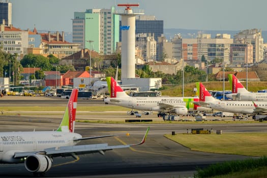 Lisbon, Portugal - Apr 24, 2024: TAP airplanes parked at Lisbon airport on sunny day with clear skies and city view in background. Planes being serviced and prepared for flights, air traffic control tower and runway, travel destination