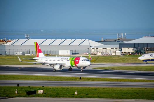 Lisbon, Portugal - Apr 3, 2024: TAP Air Portugal Airbus A321neo airplane taxiing on runway at Lisbon Airport, with hangars, airport infrastructure, clear blue sky in background. Sunny day, Ryanair waiting, vacations, summer haze, travel destination