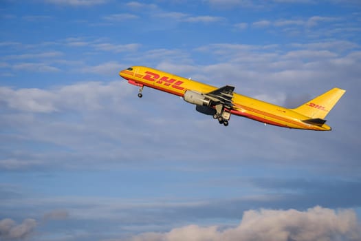 Lisbon, Portugal - Apr 3, 2024: Panning shot of DHL Boeing 757-200 cargo plane take off in Humberto Delgado Airport in blue sky with white clouds on sunny day. Shot mid-flight, aircraft, air freight, international shipment, cargo operations