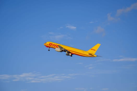 Lisbon, Portugal - Apr 3, 2024: Panning shot of DHL Boeing 757-200 cargo plane take off in Humberto Delgado Airport in blue sky with white clouds on sunny day. Shot mid-flight, aircraft, air freight, international shipment, cargo operations