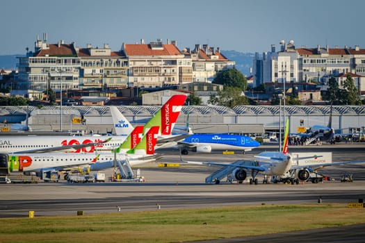 Lisbon, Portugal - Apr 24, 2024: TAP and KLM airplanes in Lisbon airport ready for boarding and takeoff on sunny day, clear blue sky. Ground support vehicles and airport Terminal 2 infrastructure, city buildings in background.