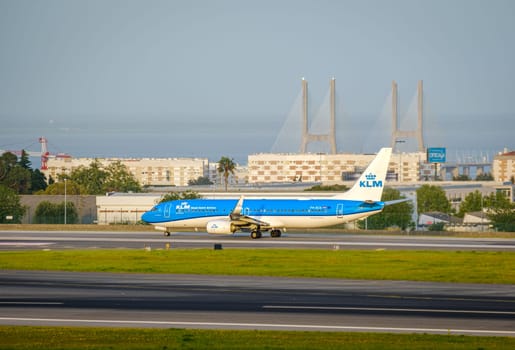 Lisbon, Portugal - Apr 3, 2024: KLM Royal Dutch Airlines aircraft Cityhopper Embraer E190 taxiing on runway at Lisbon airport on sunny day, clear sky and Vasco da Gama bridge in background. Vacations, weekend getaway, summer travel destination