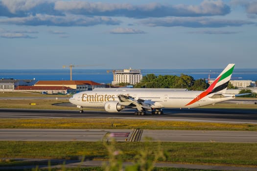 Lisbon, Portugal - Apr 3, 2024: Emirates Airline Boeing 777-300ER aircraft taxiing on runway at Lisbon airport on sunny day, clear blue sky with some clouds. Vacations, long-haul flights, travel destination, international hub, river view, cityscape