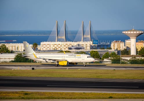 Lisbon, Portugal - Apr 3, 2024: Vueling airline Airbus A321-231 aircraft taxiing on runway at Lisbon airport on sunny day, clear sky and bridge in background. Vacations, weekend getaway, summer travel destination, international hub, takeoff, landing