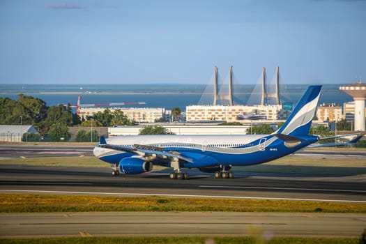Lisbon, Portugal - Apr 3, 2024: HiFly Malta Airline Airbus 330-300 airplane taxiing on runway at Lisbon airport on sunny day, clear sky and bridge in background. Vacations, weekend getaway, summer travel destination, river, aircraft takeoff, landing