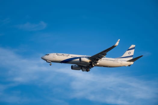 Lisbon, Portugal - Jan 14, 2025: El Al Airlines Boeing 737 shot mid-flight with landing gear extended, ready for landing on sunny day with clear blue sky and some soft clouds. Classic livery of Israel flag carrier.