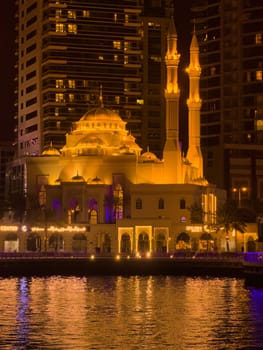 UAE, Dubai, 10 December 2024: Mosque of Muhammad Ibn Ahmad Al-Mullah against the backdrop of skyscrapers at night in Dubai Marina, yachts sailing by, reflection of night lighting on the water. High quality photo