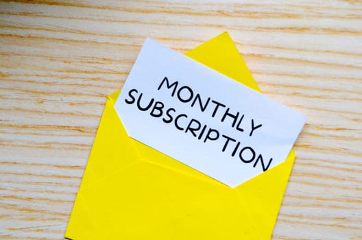 Monthly Subscription text on white notepad inside a yellow envelope. Online marketing concept.
