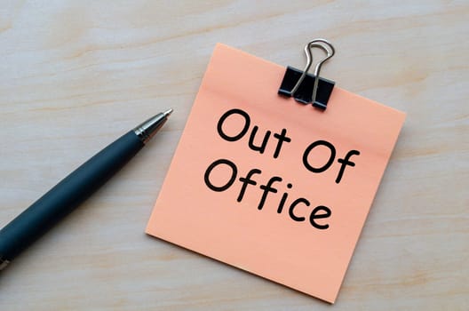Top view of out of office text on notepad on wooden table.