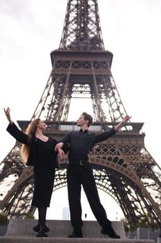 A stylish couple performs an elegant dance pose in front of the Eiffel Tower in Paris. Their graceful movements and synchronized posture capture a sense of romance and artistry.