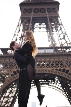 A romantic couple shares an intimate moment in Paris. The man lifts the woman in a loving embrace beneath the Eiffel Tower, symbolizing passion, connection, and the magic of love.