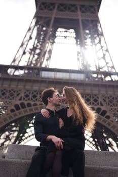 A young couple sits closely in front of the Eiffel Tower, gazing into each other eyes with love. The golden sunlight enhances their intimate and romantic moment in Paris.