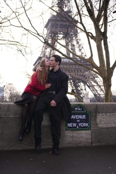 A young couple enjoys a romantic moment on Avenue de New York in Paris, with the Eiffel Tower towering behind them. The woman leans in for a kiss, capturing an intimate and stylish scene.
